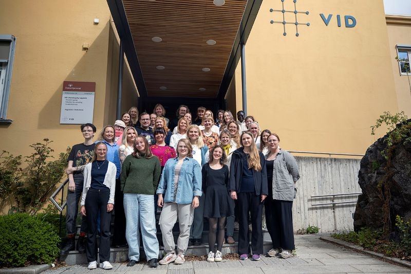 large-group-of-smiling-men-and-women-on-steps-outside-an-ochre-coloured-building